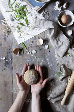 hands holding bread dough over table with rolling pin and ingredients