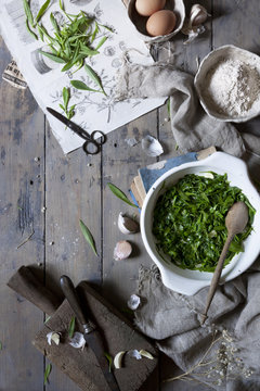 cooked seasonal wild herbs on rustic kitchen table with ingredients and tools