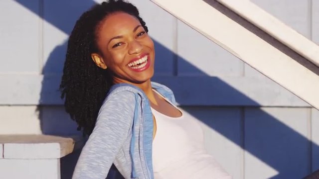 Happy black woman sitting on outdoor stairs laughing