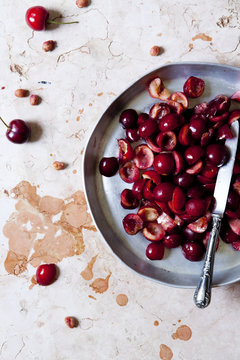 cutting in half juicy cherries on a round tray on marble surface with a knife