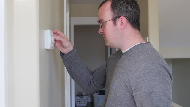 A man raises the temperature on thermostat in cold house