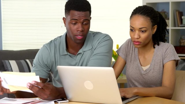 Worried young African American couple looking through bills online