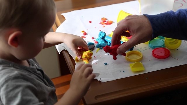 a pregnant mother and her toddler boy play with playdough on a small table dolly shot