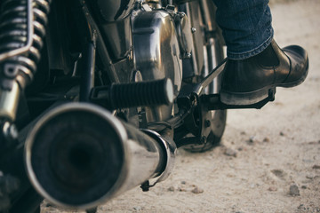 Foot of a man sitting on his motorbike on a dirt road