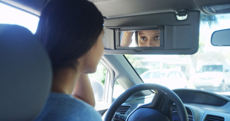 Young woman sitting in car checking her makeup in mirror