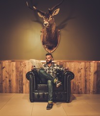 Middle-aged hipster reading newspaper on leather chair 