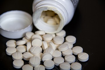 Round White tablets (medcine or food suplier) out of bottle on black background