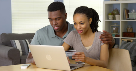 Smiling young black couple using credit card to make online purchase