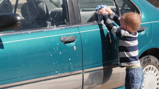 A toddler helping his mother wash a car