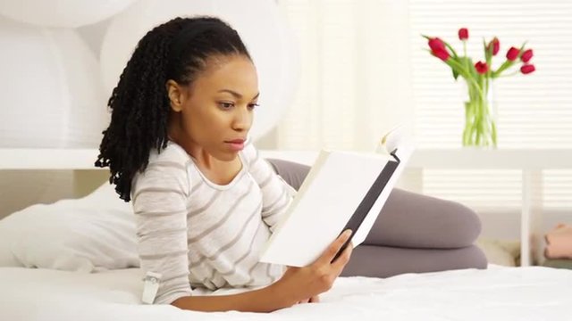 Pretty young black woman reading on bed