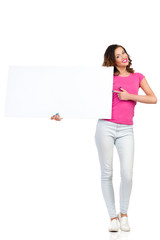 Smiling young woman holding white placard and pointing. Full length studio shot isolated on white