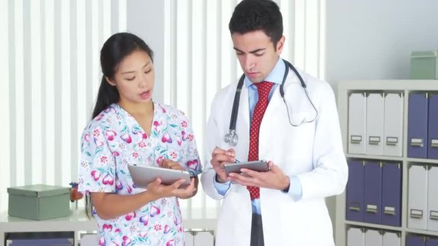 Hispanic doctor talking with Asian nurse with tablets