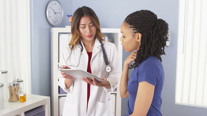 Japanese doctor talking to black patient about neck pain using tablet