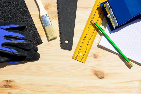Workplace and tools of a carpenter or builder.Hand saw, ruler, brush, notebook, pencil, sandpaper, and work gloves