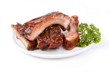 Plate of Barbecued Spareribs – Barbecued, grilled pork spareribs on a white plate. Parsley on the right side. On a white background.