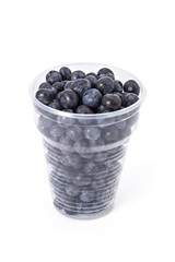 Fresh ripe organic blueberries in a plastic glass on a white background