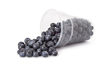 Plastic glass and spilled fresh ripe organic blueberries on a white background