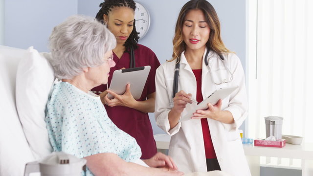 Asian doctor and African American nurse speaking with mature woman patient
