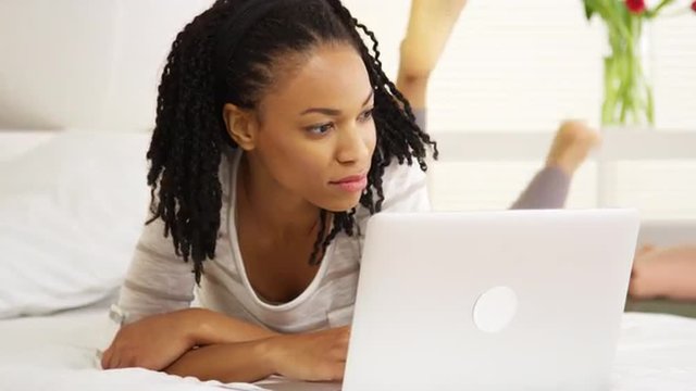 Smiling black woman using laptop on bed