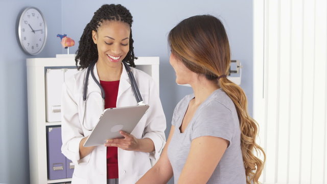Black doctor with tablet talking to female Asian patient