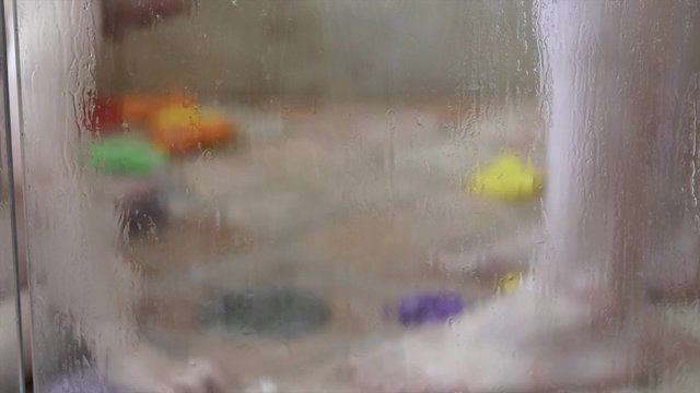 A toddler plays with toys in the shower with his mom