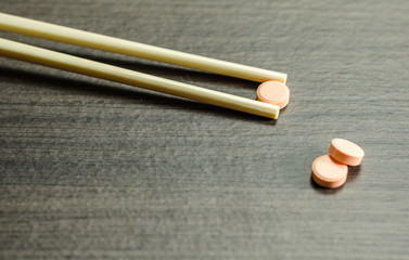 Chopsticks picking up medicine tablet on a table