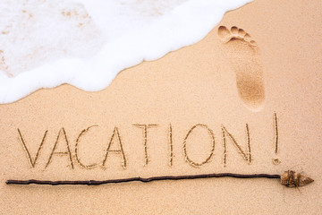 Inscription of Vacation written on wet yellow beach sand with fo