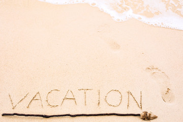 Inscription of Vacation written on wet yellow beach sand with fo