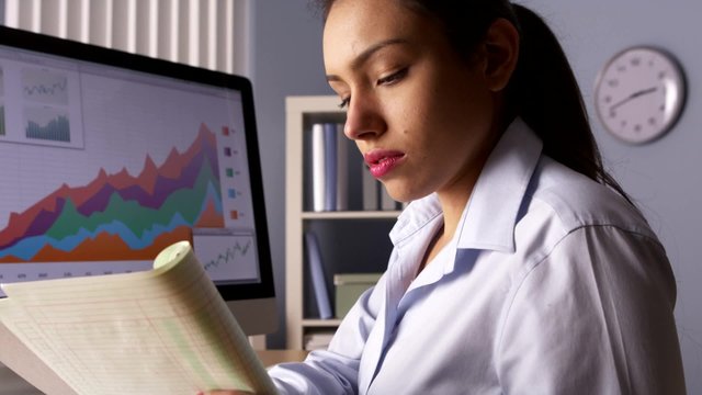 Hispanic businesswoman writing notes by computer