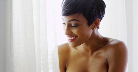 Topless black woman looking out window and smiling