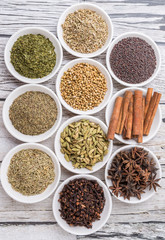 Cardamom, star anise, cinnamon, clove, coriander seed spices and parsley, thyme, rosemary herbs in white bowls 