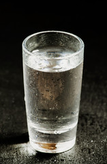 Glass with a transparent drink on dark background, black and whi