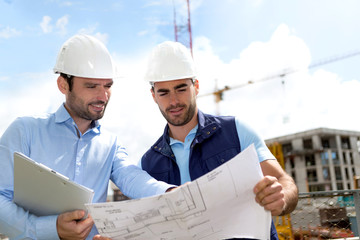 Engineer and worker checking plan on construction site - obrazy, fototapety, plakaty
