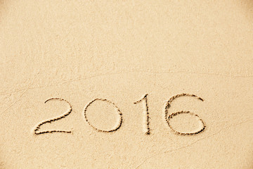 2016 inscription written in the wet yellow beach sand