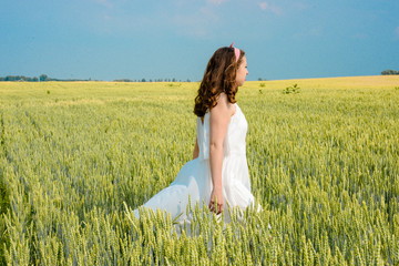 A beautiful young woman on a wheat field. Stylish brunette girl with red lips standing in the field on a sunny day. Concept of freedom and happiness 