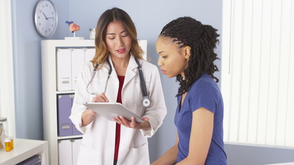 African American patient explaining issues to Asian doctor using tablet - Powered by Adobe