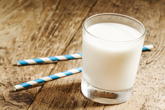 A glass of fresh milk with striped blue and white tubes on an ol