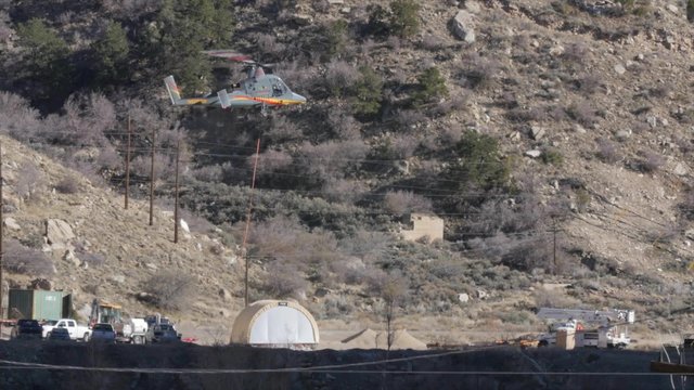 Helicopter carrying supplies decends to land in mountains