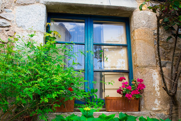 Fototapeta na wymiar Old blue wood window with flowers on the facade of stone house
