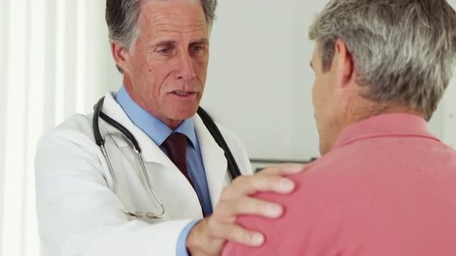 Senior doctor talking to elderly patient with hand on shoulder