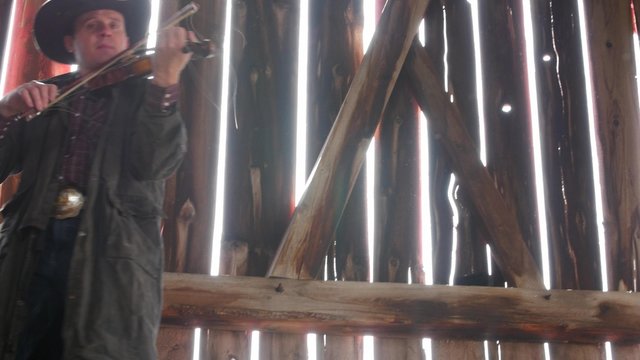 A cowboy plays old fiddle in barn rafters for a barn dance