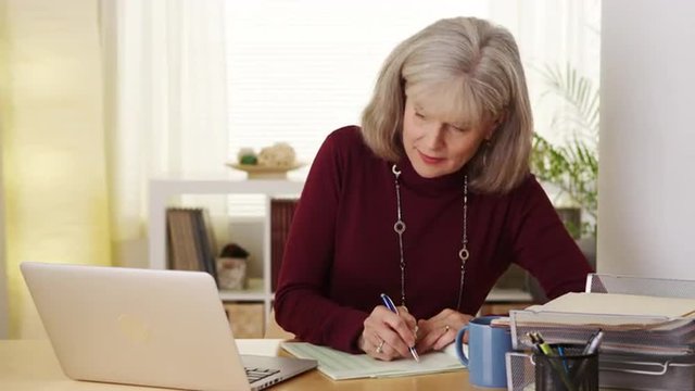 Eldery woman using laptop computer taking notes smiling