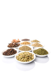 Cardamom, star anise, cinnamon, clove, coriander seed spices and parsley, thyme, rosemary herbs in white bowls 