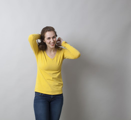 beautiful smiling 20s woman wearing yellow sweater and jeans, fixing her hair for pose with copy space