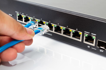 LAN network switch with ethernet cables plugging in on white