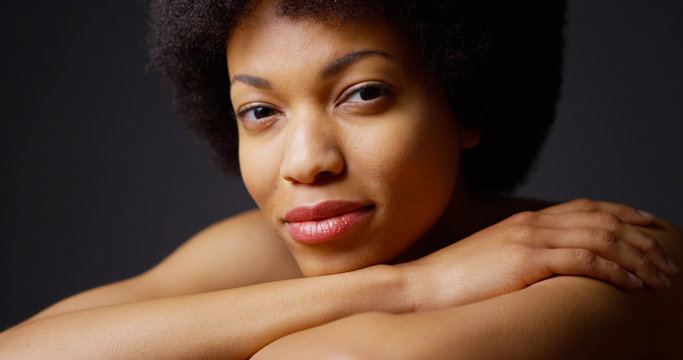 Black Woman Sitting With Arms Crossed Smiling On Grey Background