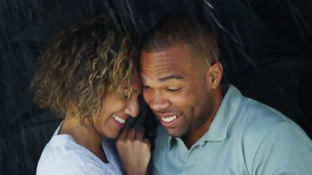 Black couple laughing under umbrella together