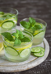 Lemonade with cucumber, lemon, mint and ginger in glass cups on a wooden surface