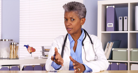 Senior african doctor sitting at desk and talking to camera