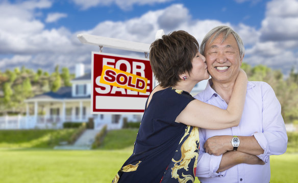 Affectionate Senior Chinese Couple In Front Of House And Sign